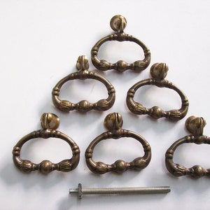 May include: Six antique brass cabinet knobs with a decorative oval design and a single screw. The knobs are arranged in a triangular pattern on a white surface.