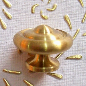 May include: A gold-toned cabinet knob with a round, slightly domed top and a short, cylindrical base.