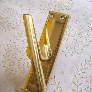 Può includere: Una maniglia per porta dorata con una piastra rettangolare e una leva curva. La maniglia ha una finitura lucida.