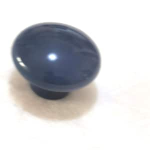 Puede incluir: Un pomo de armario azul marino en forma de huevo con un acabado brillante. El pomo está montado sobre una base cilíndrica corta. El herraje está diseñado para cajones o puertas de armarios.