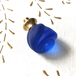Peut inclure: Un bouton en verre bleu en forme de rose avec une base en métal doré.