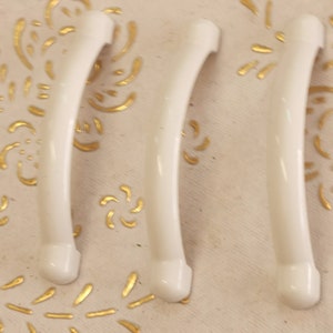 Pode incluir: Três puxadores de porta de armário de plástico branco com forma curva.