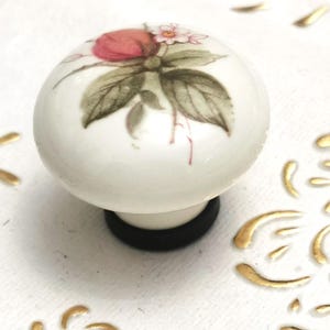 May include: White ceramic knob with a floral design featuring pink and green leaves and a white flower.