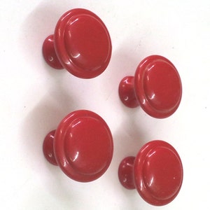 Könnte beinhalten: Vier rote Schrankknöpfe mit einem erhabenen, kreisförmigen Design. Die Knöpfe sind aus einem glatten, glänzenden Material gefertigt.