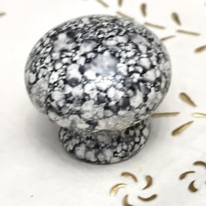 Puede incluir: Un pomo de cerámica negro y blanco moteado con una parte superior redonda y una parte inferior ligeramente redondeada.