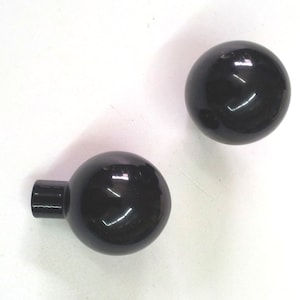Könnte beinhalten: Zwei schwarze runde Knöpfe mit glänzender Oberfläche. Der Knopf links hat einen kurzen, zylindrischen Stiel.