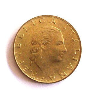 Op de afbeelding: Een gouden munt met de inscriptie "REP. ITALIANA" rond de rand en een profiel van een vrouwenhoofd in het midden.