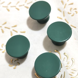 Puede incluir: Cuatro pomos de armario redondos de color verde oscuro con un acabado liso y mate.
