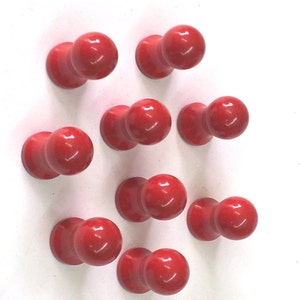 Può includere: Dieci puntine da disegno in plastica rossa con teste rotonde e una base cilindrica.