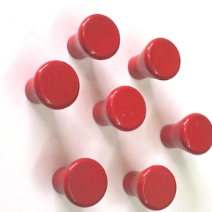 以下が含まれることがあります： 丸いトップと円筒形のベースを持つ赤い木製のノブが8つ。ノブは白い背景に円形に配置されています。