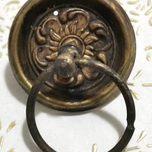 Puede incluir: Un llamador de puerta de latón vintage con un diseño floral decorativo y un tirador en forma de anillo.
