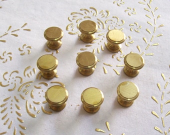 May include: Nine gold-toned cabinet knobs with a round, slightly raised top and a cylindrical base.