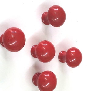 Może przedstawiać: Pięć czerwonych plastikowych gałek z okrągłym wierzchołkiem i krótką nóżką. Gałki są ułożone w półkole na białym tle.