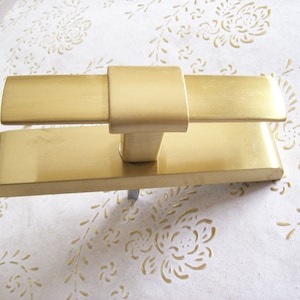 May include: Gold door handle with a rectangular plate and a square lever. The handle is made of metal and has a brushed finish.