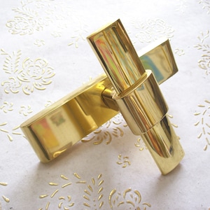 Könnte beinhalten: Ein polierter Türgriff aus Messing mit einem einzigartigen, geometrischen Design. Der Griff ist aus massivem Messing gefertigt und hat eine glatte, glänzende Oberfläche.