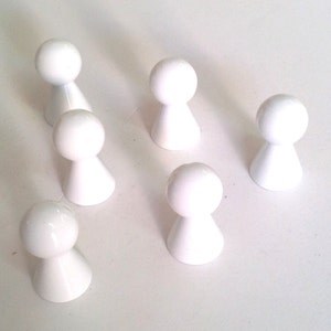 Könnte beinhalten: Sechs weiße Spielfiguren aus Kunststoff in Form von Menschen. Die Figuren stehen auf einer weißen Oberfläche.