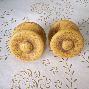 Peut inclure: Deux boutons ronds en bois pour armoire avec une finition texturée en grain de bois. Les boutons sont de couleur brun clair avec un centre brun foncé.