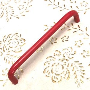 Könnte beinhalten: Ein leuchtend roter, gebogener Metallgriff. Der Griff ist ein gerader Stab mit gebogenen Enden. Der Hintergrund ist eine weiße Oberfläche mit einem goldenen Blumenmuster.