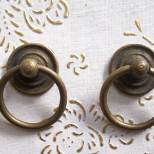 May include: Two antique brass cabinet door pulls with a ring handle and a round decorative base.