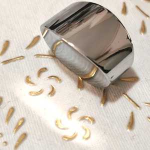 Könnte beinhalten: Ein glänzender Silberring mit einem breiten, flachen Band. Der Ring hat eine glatte, polierte Oberfläche.