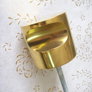 Puede incluir: Un pomo de metal dorado con la parte superior redondeada y un tornillo roscado. El pomo está diseñado para muebles o puertas de armarios.