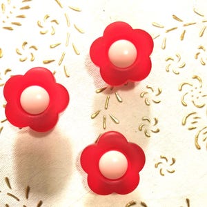 May include: Three red plastic flower-shaped buttons with white centers.