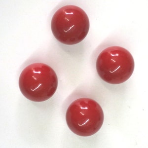 Może przedstawiać: Cztery błyszczące, okrągłe, czerwone koraliki ułożone na białej powierzchni. Każdy koralik odbija światło, podkreślając ich gładki, kulisty kształt. Koraliki są równomiernie rozmieszczone, tworząc symetryczny wzór.