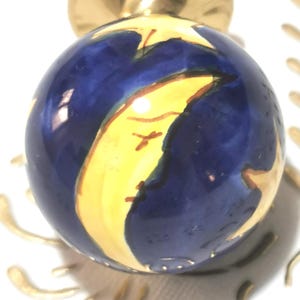 Op de afbeelding: Een decoratieve kastknop met een hemels ontwerp. De knop heeft een marineblauwe bol met een gele maan en sterren. De basis en de bovenkant van de knop zijn goudkleurig.