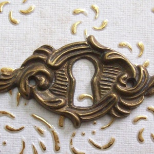 Puede incluir: Una tapa de mirilla de latón con un diseño decorativo y ornamentado. La tapa tiene una mirilla en el centro y espirales y curvas intrincadas alrededor de los bordes.