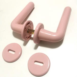 May include: Two pale pink door handles and matching round backplates. The handles have a curved design and are made of a solid, smooth material. The backplates have a slot for the keyhole. The hardware is new and unused.