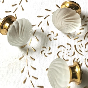 Può includere: Tre pomelli per armadi in vetro bianco con un design a spirale e basi in metallo dorato.