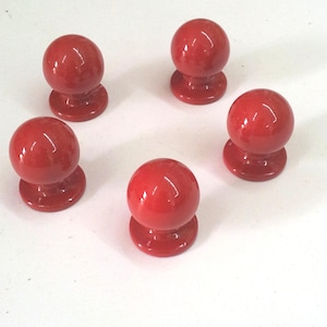Pode incluir: Cinco botões de armário de cerâmica vermelha com forma redonda e acabamento liso e brilhante.