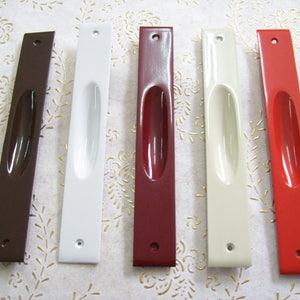 Puede incluir: Cinco tiradores de puerta en diferentes colores: marrón, blanco, rojo, beige y naranja. Los tiradores son de metal y tienen una forma rectangular con un tirador ovalado empotrado.