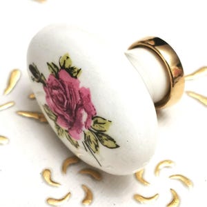 Può includere: Pomo per cassetti in ceramica bianca con un design a rosa rosa e una base in metallo dorato.