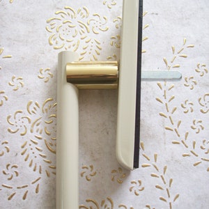 May include: A white and gold window handle with a black rubber seal. The handle has a long, straight lever and a round, gold knob.