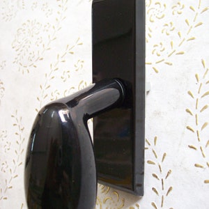 May include: A black door handle with a rounded, oval-shaped lever. The handle is mounted on a rectangular plate.