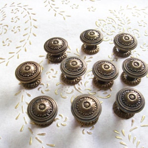 Könnte beinhalten: Zehn antike Messing-Schrankknöpfe mit floralem Design. Die Knöpfe sind rund und haben eine erhabene Mitte mit einem floralen Muster.