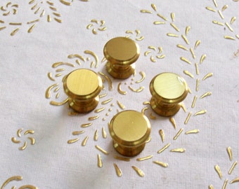May include: Four gold-toned round cabinet knobs with a smooth, shiny finish. The knobs are arranged in a square pattern on a white surface.