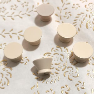 以下が含まれることがあります： 丸みを帯びたトップとわずかに盛り上がったベースを持つ、オフホワイトのセラミックノブが6つ。1つのノブは、円錐形のトップを持つ異なる形状です。