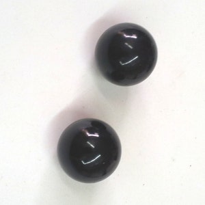 Puede incluir: Dos bolas redondas negras y brillantes sobre un fondo blanco.