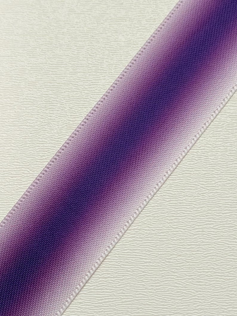Pu&ograve; includere: Un nastro viola diagonale con un effetto sfumato, che passa da un viola intenso a una tonalit&agrave; lavanda pi&ugrave; chiara. Il nastro ha un bordo cucito ed &egrave; posto su uno sfondo bianco sporco strutturato. Ideale per l'artigianato e l'incarto regali.
