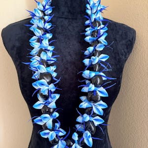 Pu&ograve; includere: Una collana lei con pietre nere alternate e accenti floreali blu e bianchi. La lei &egrave; esposta su un manichino nero, mettendo in risalto i colori vivaci e il design floreale.