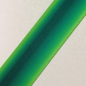 Pu&ograve; includere: Un nastro verde diagonale con un effetto sfumato, che passa da tonalit&agrave; di verde scuro a chiaro. I bordi sono cuciti con cura con un filo verde pi&ugrave; chiaro, creando un bordo definito. Il nastro viene probabilmente utilizzato per l'artigianato o l'incarto regalo.