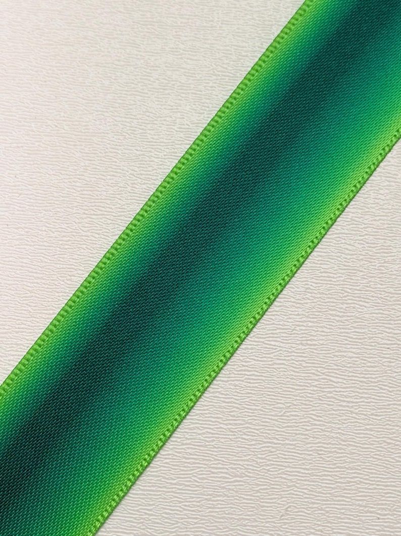 Pu&ograve; includere: Un nastro verde diagonale con un effetto sfumato, che passa da tonalit&agrave; di verde scuro a chiaro. I bordi sono cuciti con cura con un filo verde pi&ugrave; chiaro, creando un bordo definito. Il nastro viene probabilmente utilizzato per l'artigianato o l'incarto regalo.