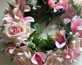 May include: A pink and white flower lei with green leaves. The lei is made of roses and orchids.