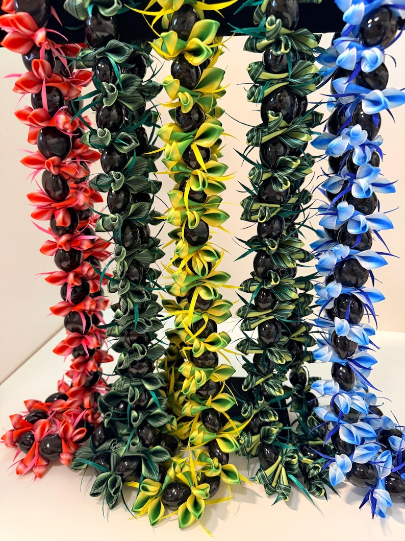 Pu&ograve; includere: Una collezione di collane di fiori colorate, ognuna con una combinazione unica di nastri vibranti e perline scure e rotonde. Le collane sono esposte in tonalit&agrave; di rosso, verde, giallo e blu, creando una disposizione visivamente sorprendente e festosa.