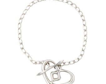 Pode incluir: Pulseira prateada com um pendente em forma de coração. O pendente tem um design aberto com um detalhe geométrico e está ligado a uma pulseira de corrente. A pulseira é feita de um material metálico brilhante.