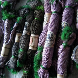 May include: A collection of colorful embroidery floss spools with different colors and patterns. The spools are wrapped in various shades of purple, green, black, and brown. The spools have labels with text that includes the number 300 and the words "Mill Hill" and "All Purpose".