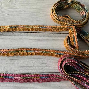 May include: Three different trims of colorful, beaded, and embroidered fabric ribbon. The trims are in shades of pink, green, blue, and gold.
