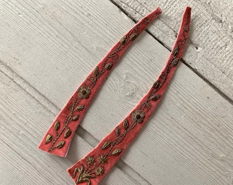 May include: Two long, narrow strips of pink velvet fabric featuring intricate gold-toned metallic thread embroidery. The embroidery depicts a continuous vine pattern with small leaves and flowers running along the length of each strip.